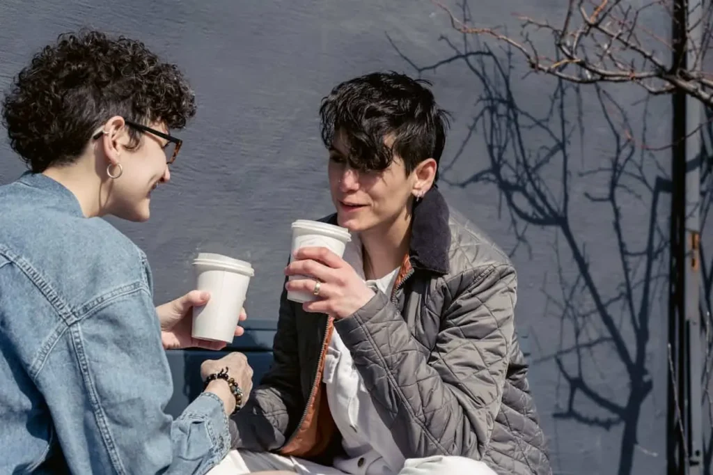 Two friends are chatting and smiling while holding cups of coffee