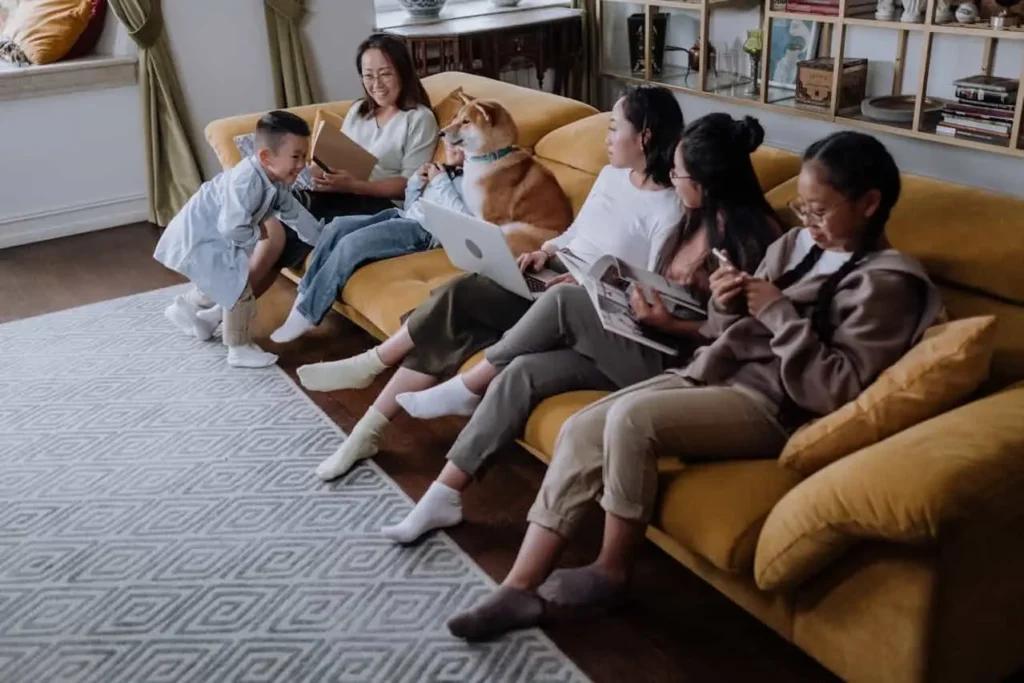 Four teenage girls are sitting on a sofa, holding a laptop and chatting with each other in a cheerful mood