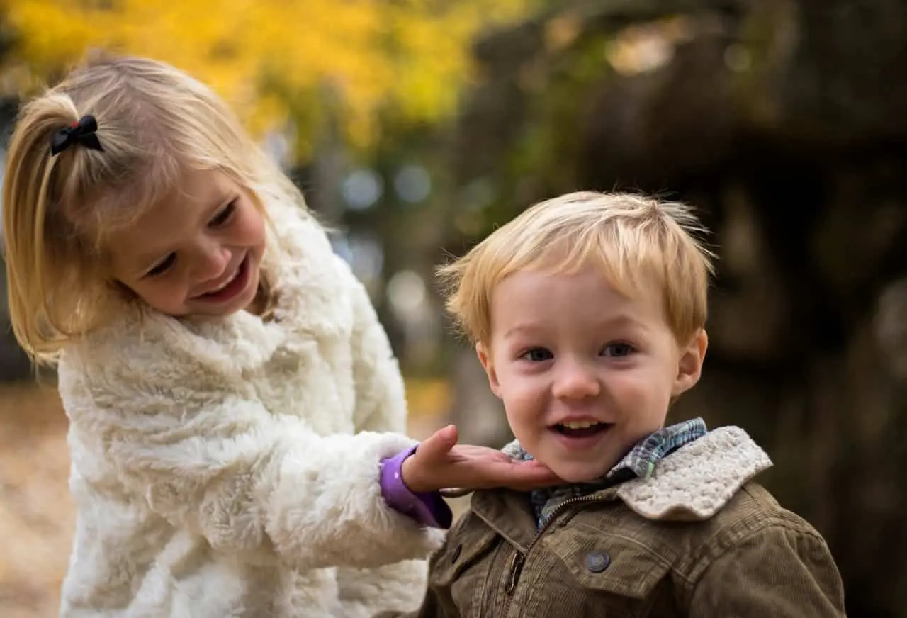 Two small kids; brother and sister are smiling and looking happy after resolving conflict