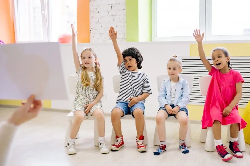 Four children raise their hands to answer questions and actively participating in morning meeting questions.